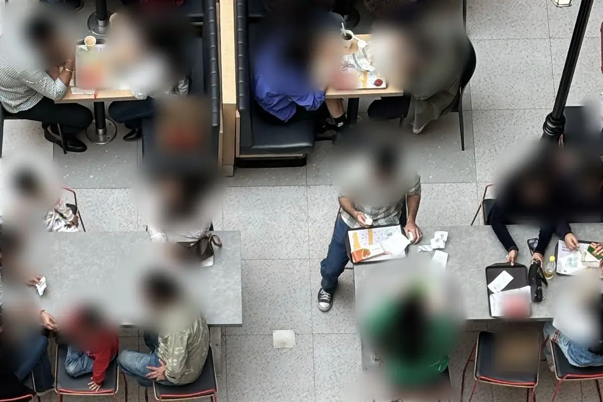 Yukarıdan çekilmiş kalabalık bir yemek alanı: masalarda oturan misafirler. Yüzler bulanıklaştırılmış.